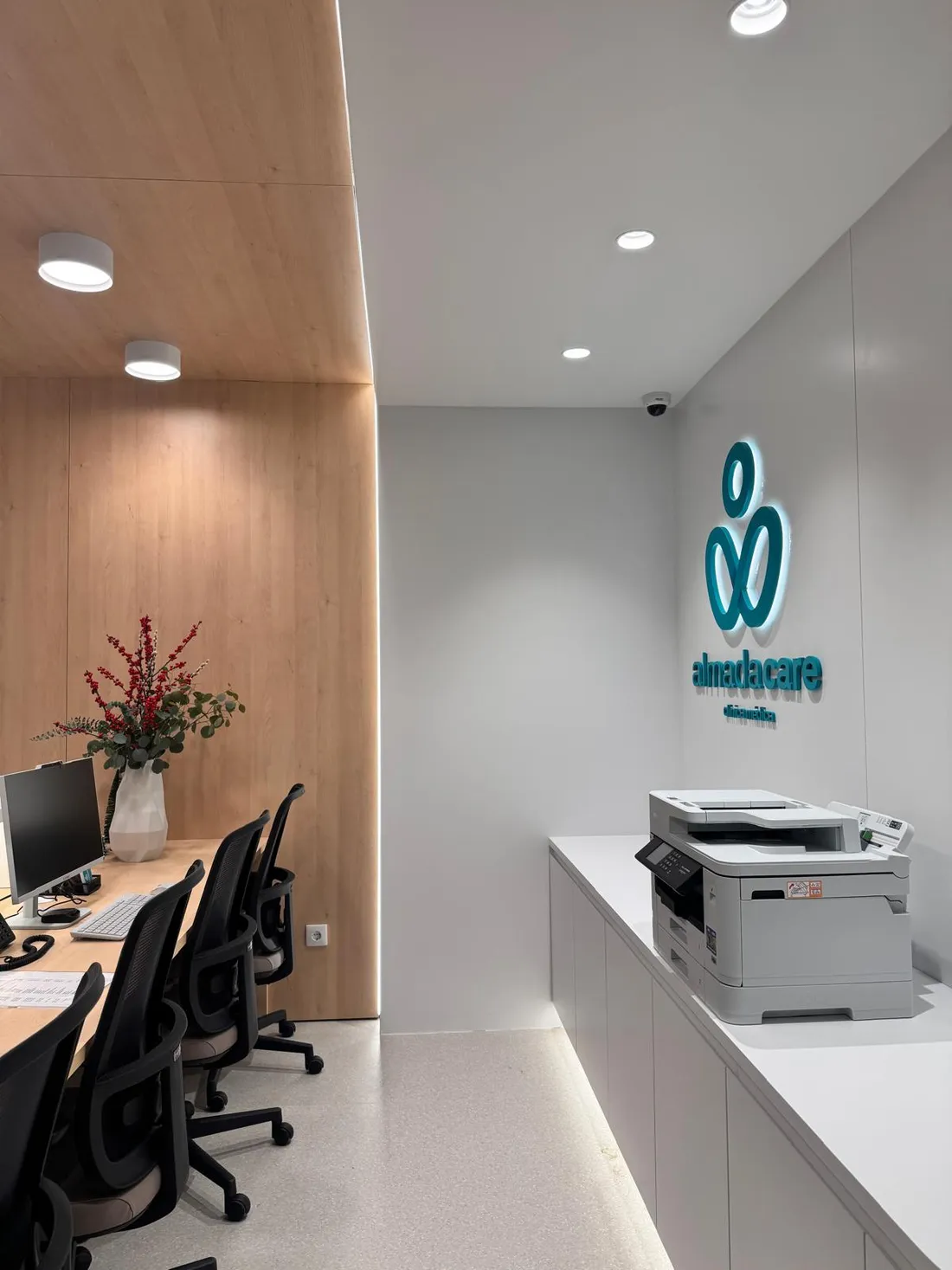 Balcão de receção da Clínica Almada Care, em madeira clara com o logótipo turquesa.