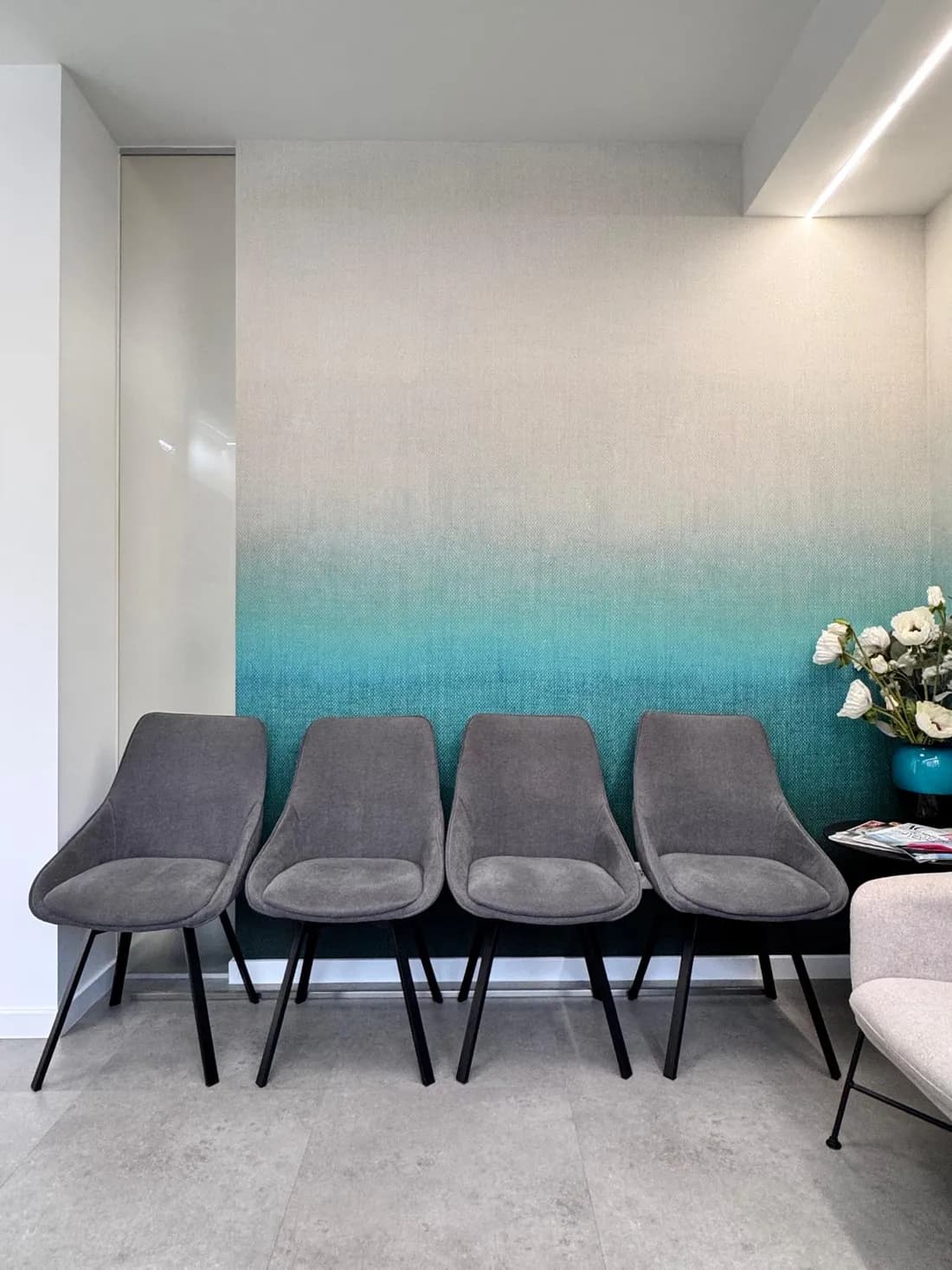 Sala de espera com cadeiras alinhadas junto à parede em degradê turquesa.
