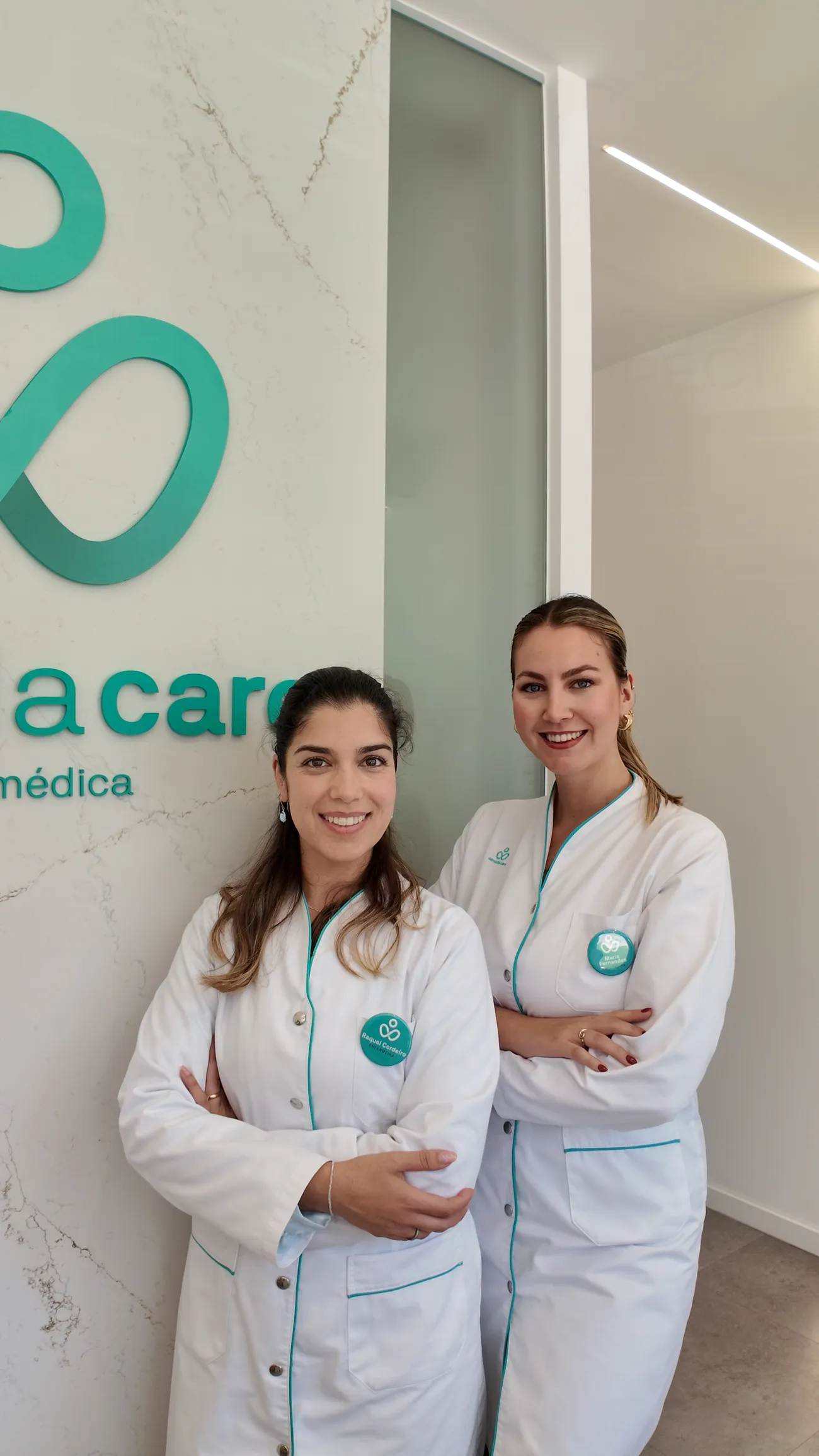 Duas profissionais da Almada Care a sorrir junto à parede de mármore.